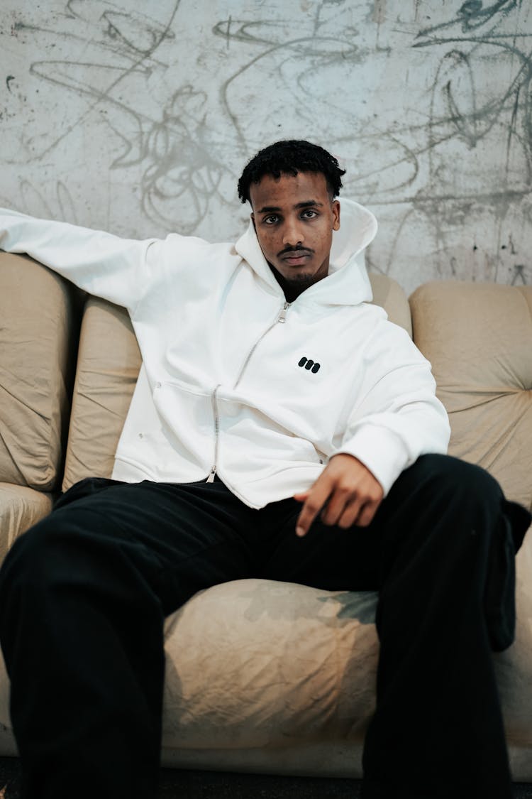 Young Man Wearing A White Hoodie And Sitting On A Sofa 