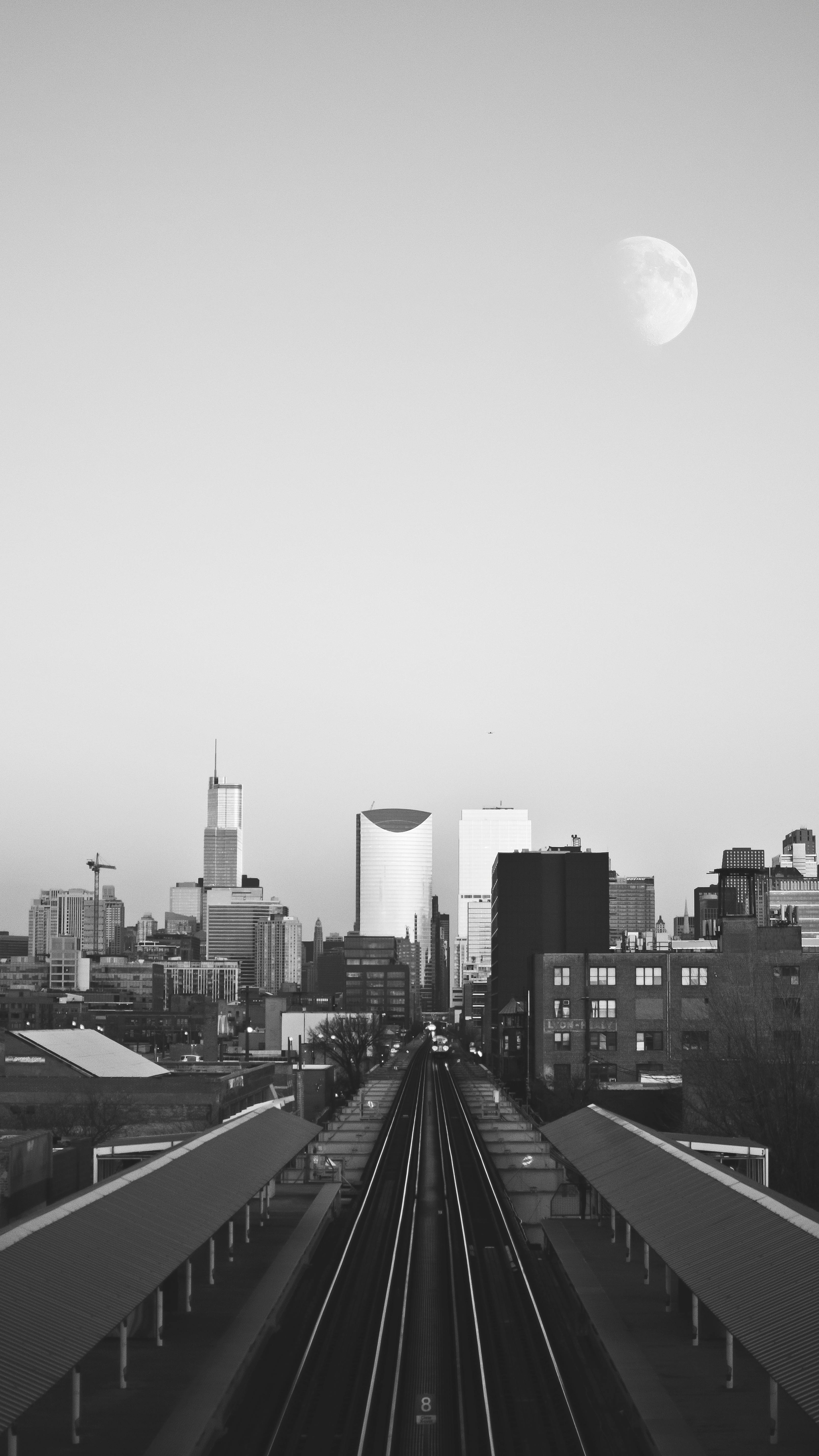 A dramatic grayscale view of Chicago skyline featuring the moon and railroad tracks.