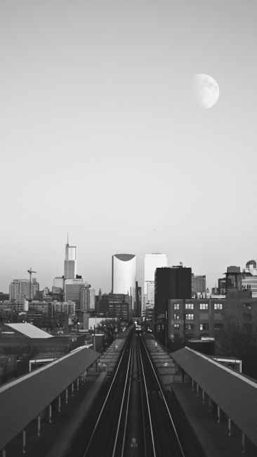 A dramatic grayscale view of Chicago skyline featuring the moon and railroad tracks.