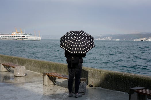 Woman with a polka dot umbrella standing by the sea, watching cruise ships pass.