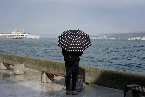 Free Woman with a polka dot umbrella standing by the sea, watching cruise ships pass. Stock Photo