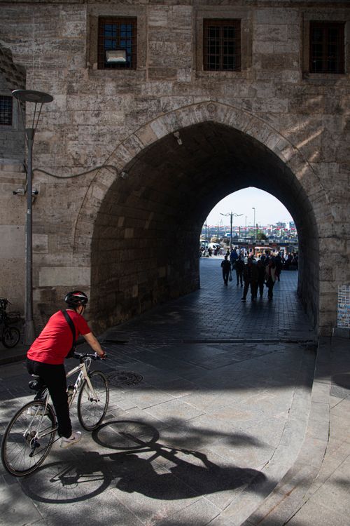 Free Cyclist enters historical stone archway in Istanbul, near Yeni Camii mosque. Stock Photo