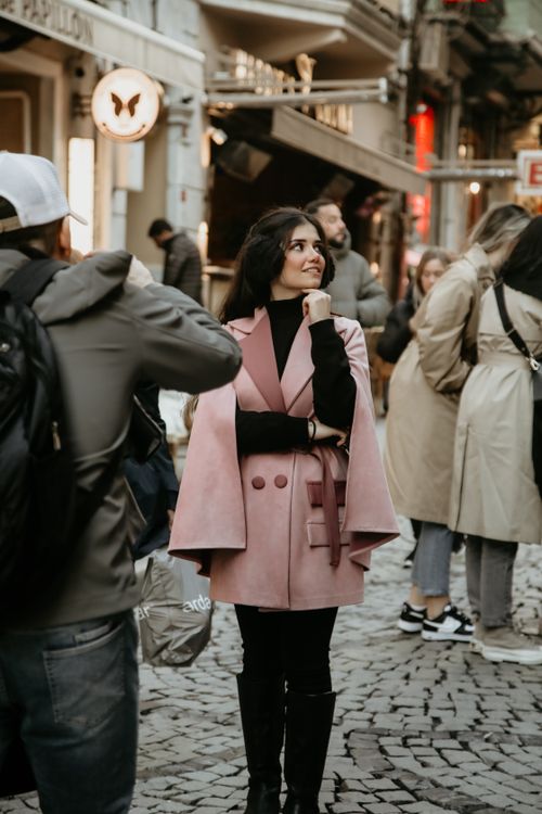 Free Woman in pink coat stands on a bustling Istanbul street, surrounded by city life. Stock Photo