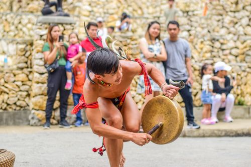 Free A teenager in traditional attire energetically plays a drum during a festival, engaging an audience. Stock Photo