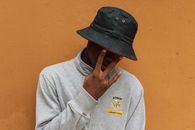 Close-up portrait of a young man posing indoors with a casual outfit and hat.