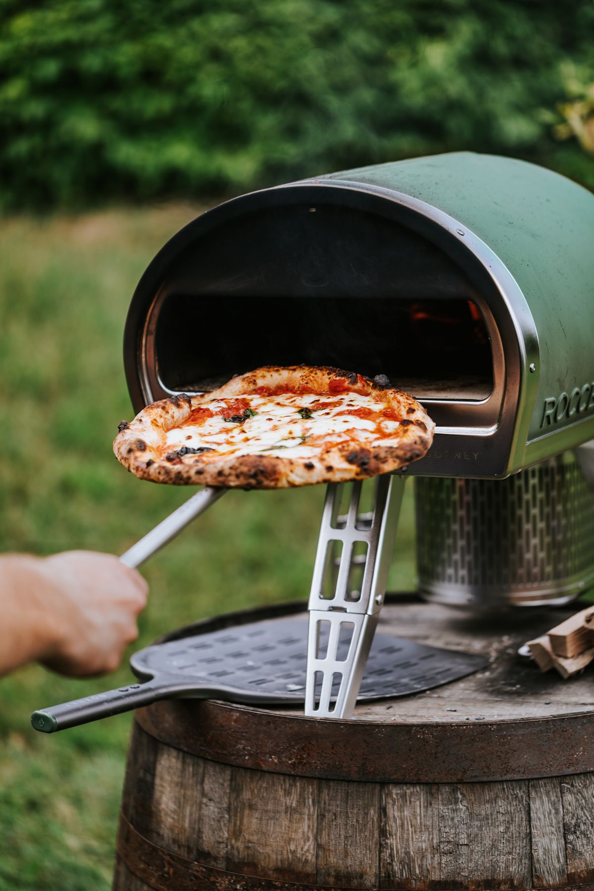 Wood-fired pizza coming out of an outdoor oven
