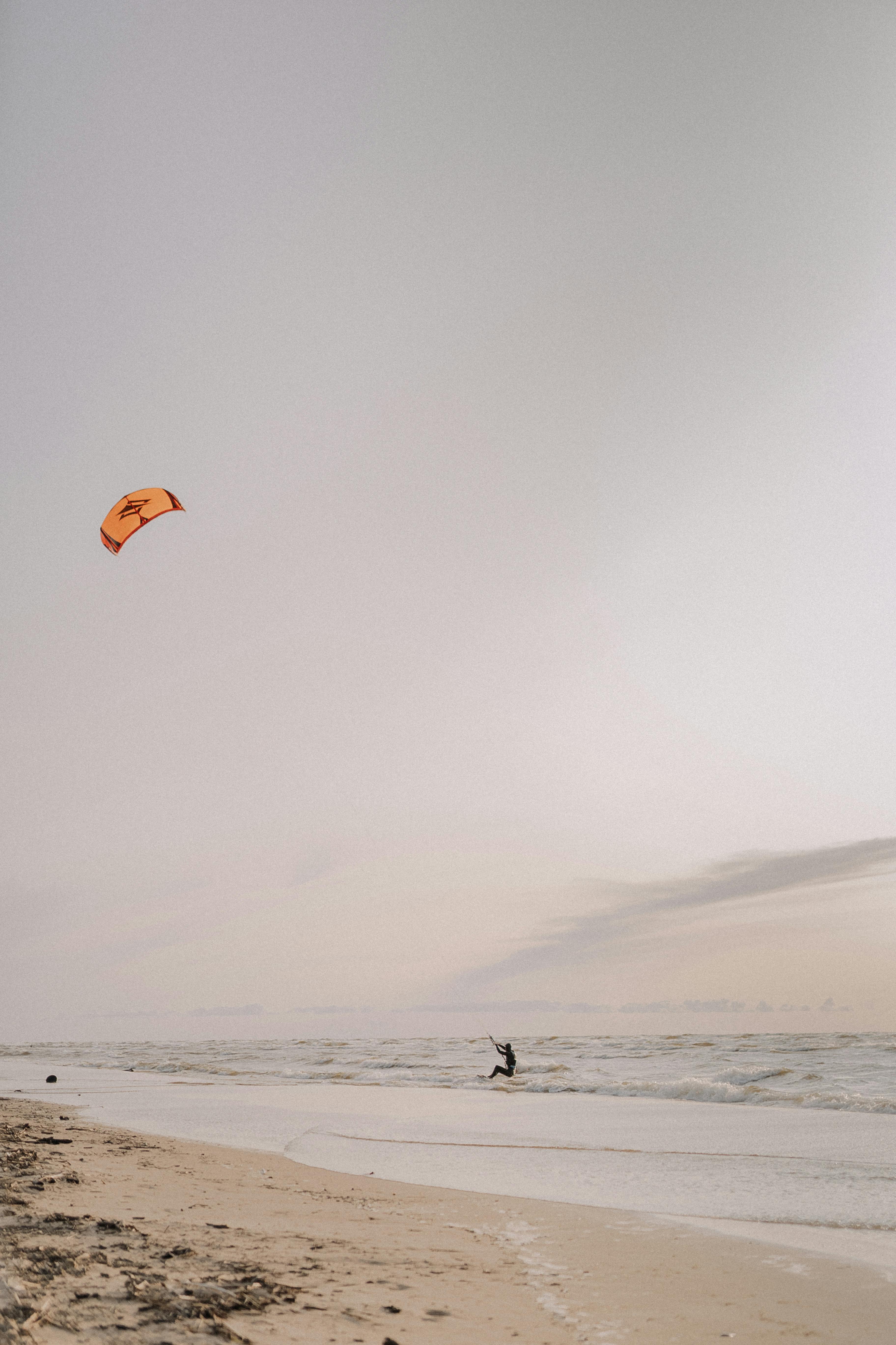 A kitesurfer skillfully glides along the shoreline during a picturesque sunset.