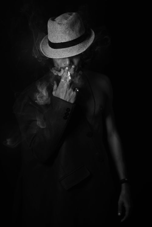 Free Black and white portrait of a man in a suit and hat smoking, exuding mystery. Stock Photo