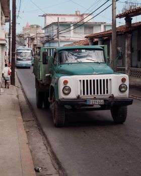 Classic green truck on city street with urban architecture backdrop.