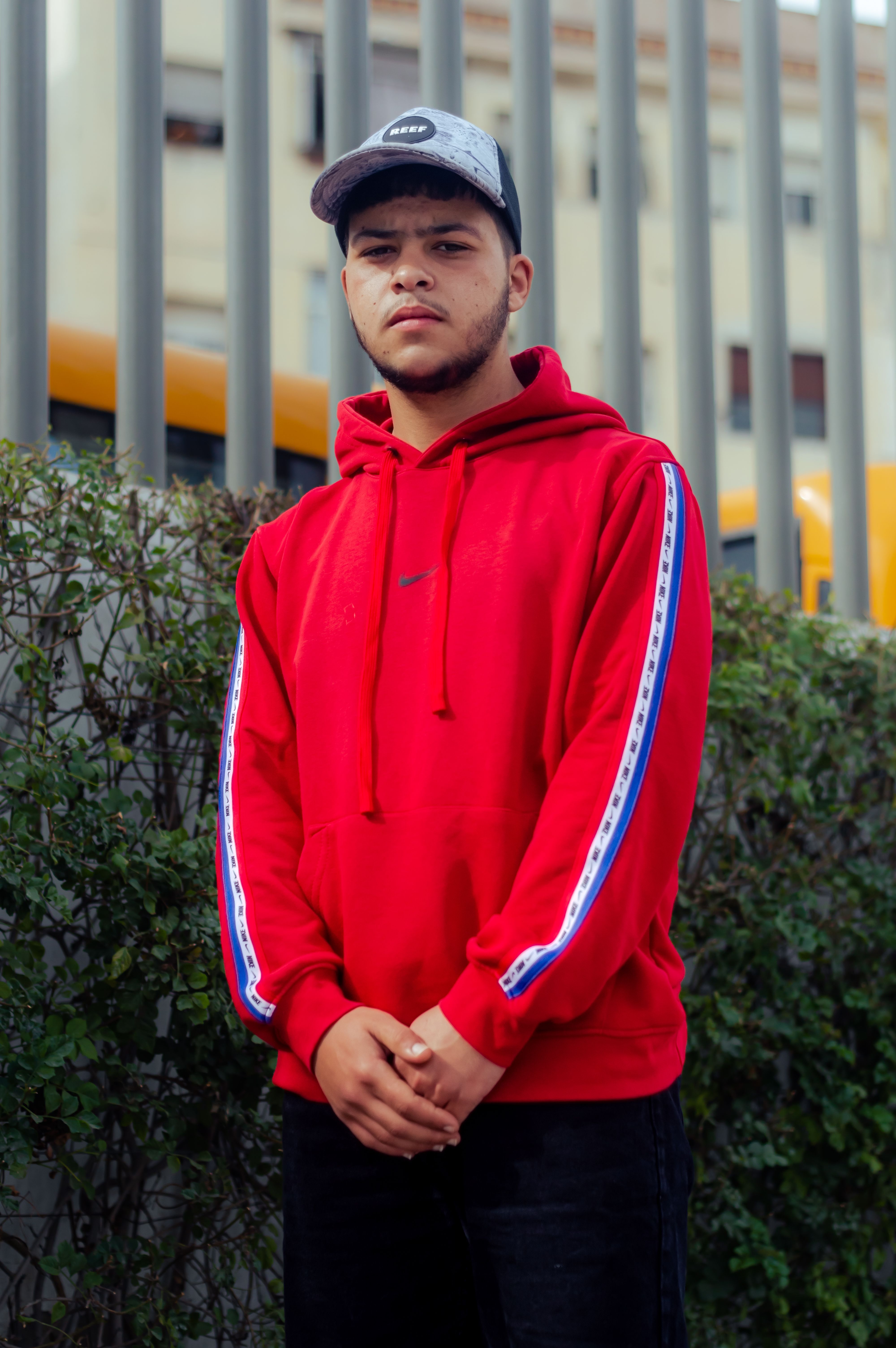 Stylish portrait of a man in a red hoodie shot outdoors in an urban setting.