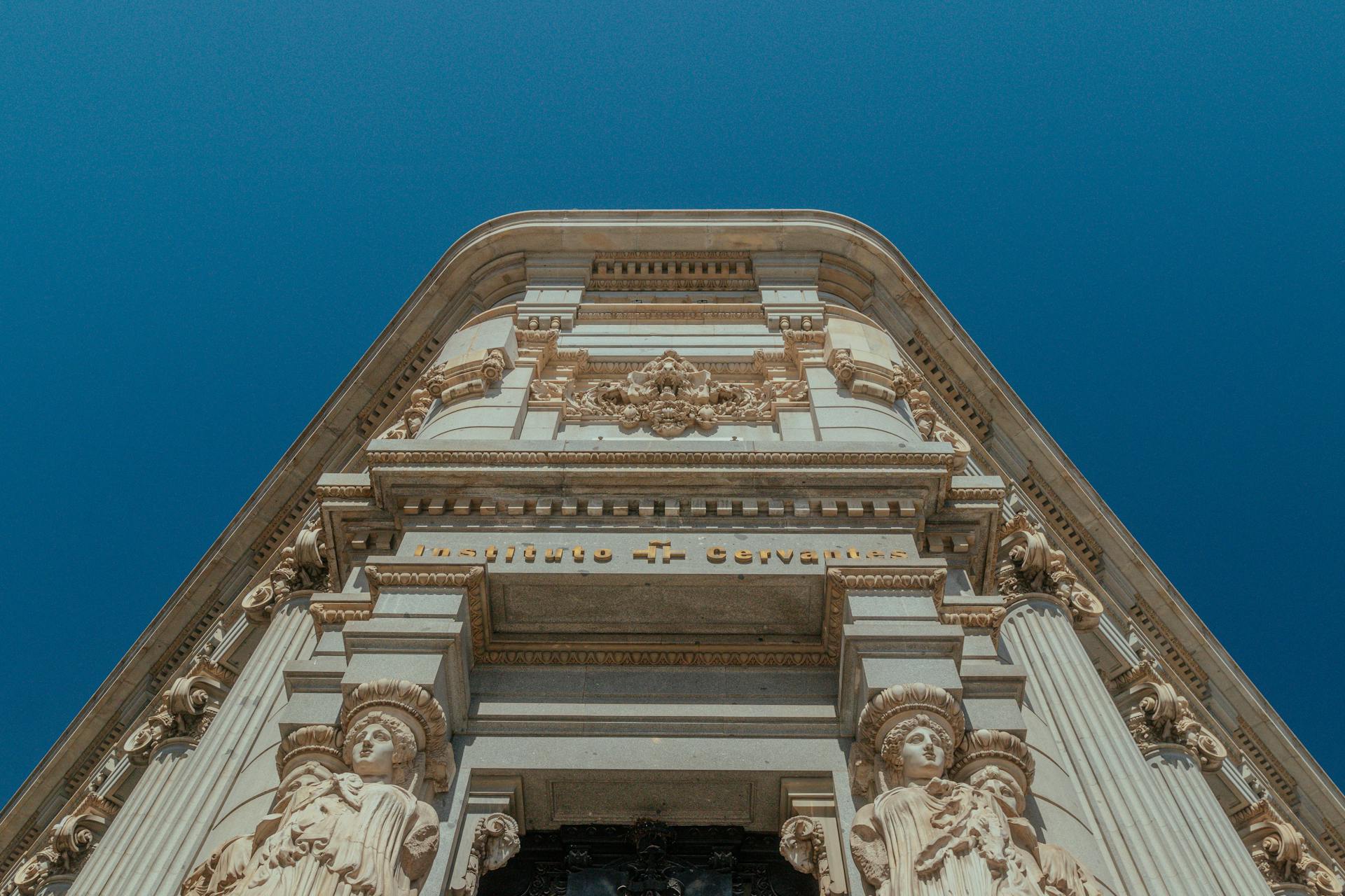 Ornate architecture of Instituto Cervantes with sculptures, set against a clear blue sky.