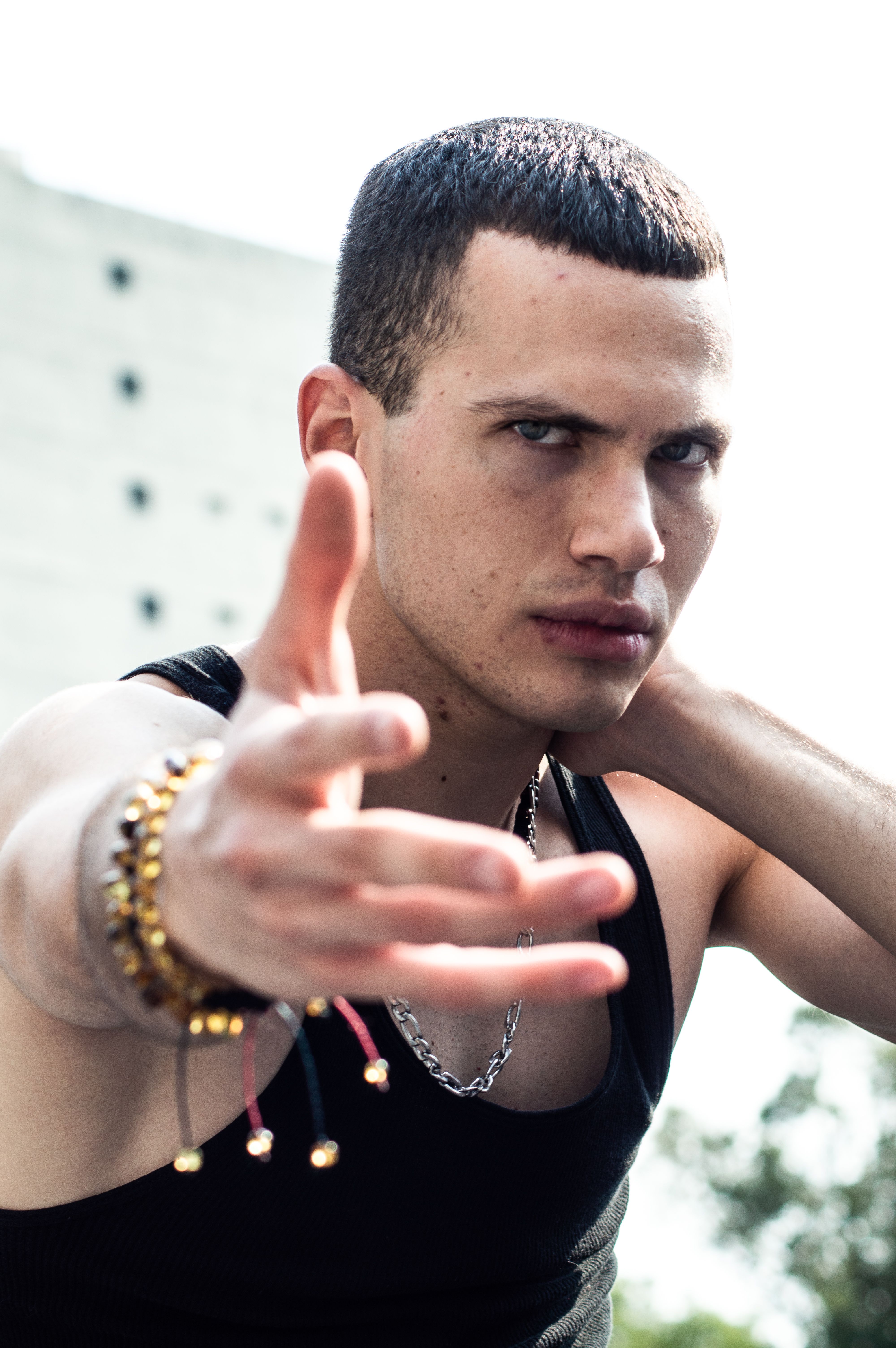 Young man in a tank top gesturing confidently outdoors, showcasing style and attitude.