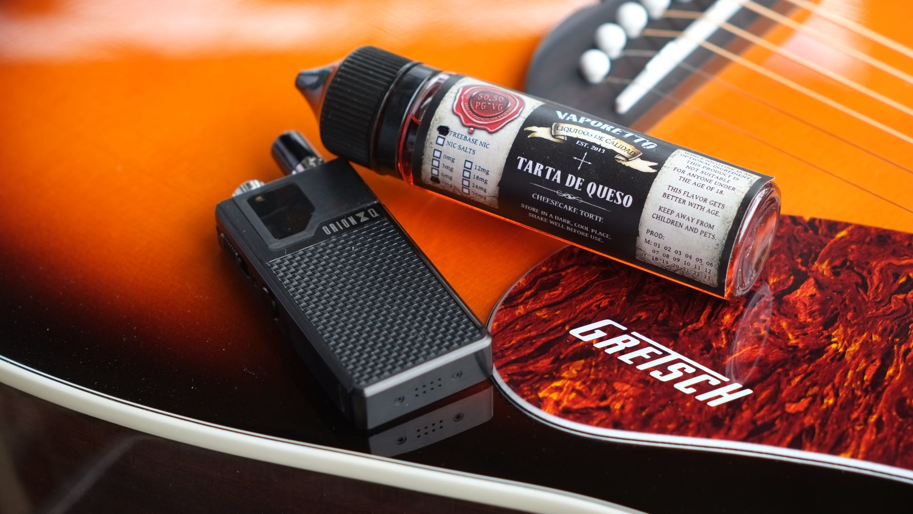 Close-up of an electronic cigarette and liquid bottle on an orange acoustic guitar.