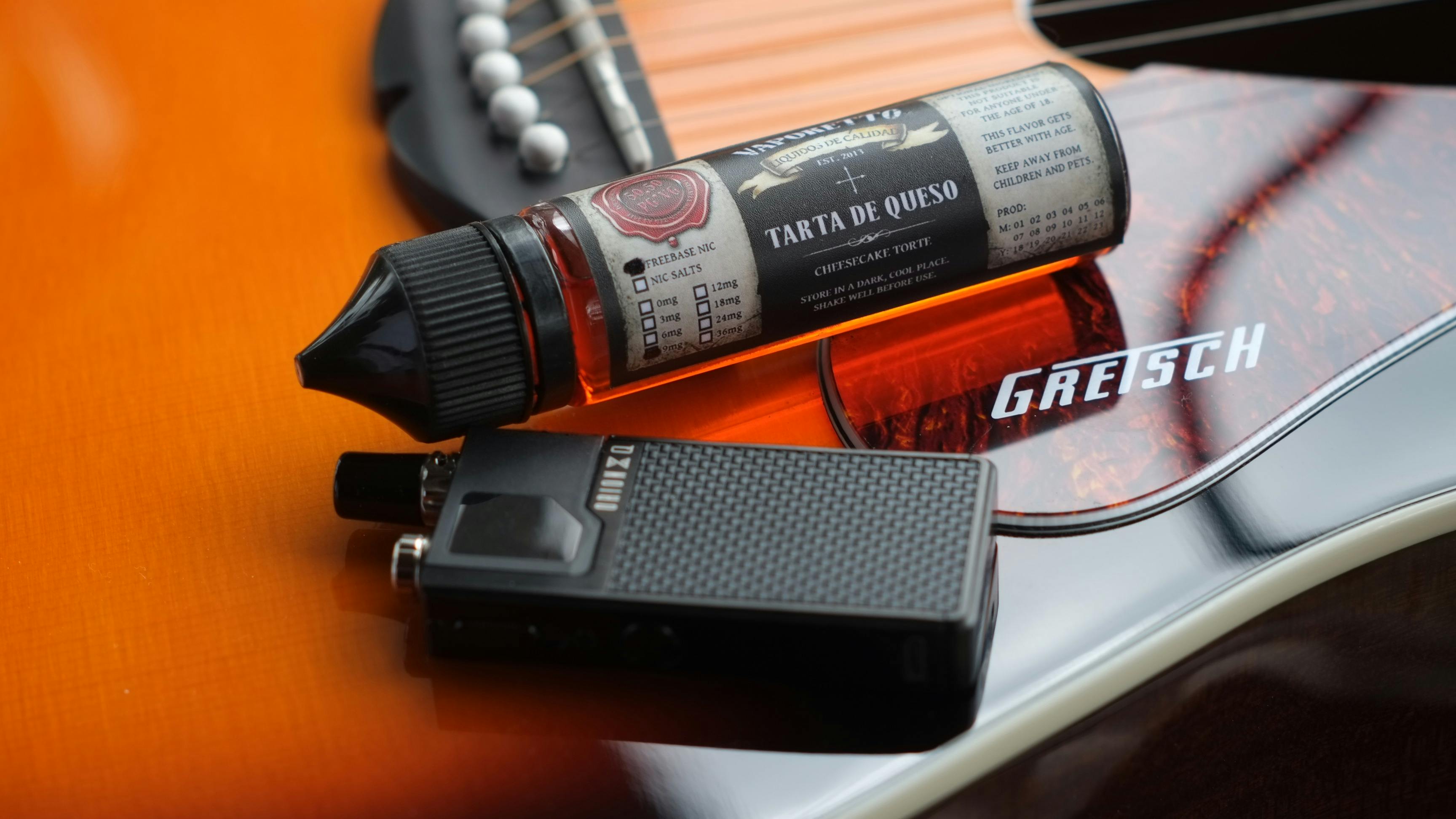 vape and cheesecake flavored liquid cartridge lying on a guitar