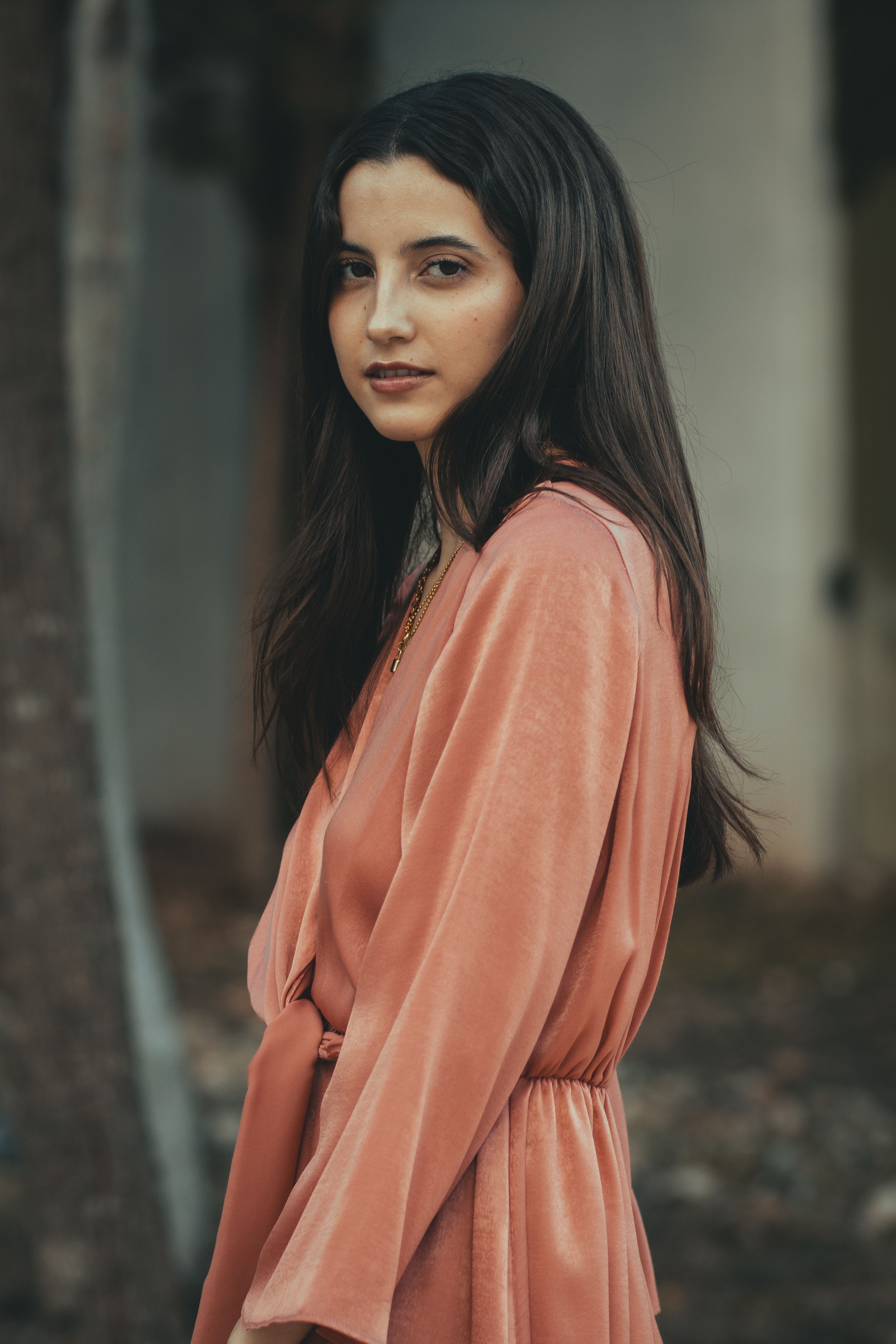 Portrait of a woman with long hair posing outdoors in a flowing peach dress, embracing soft natural light.