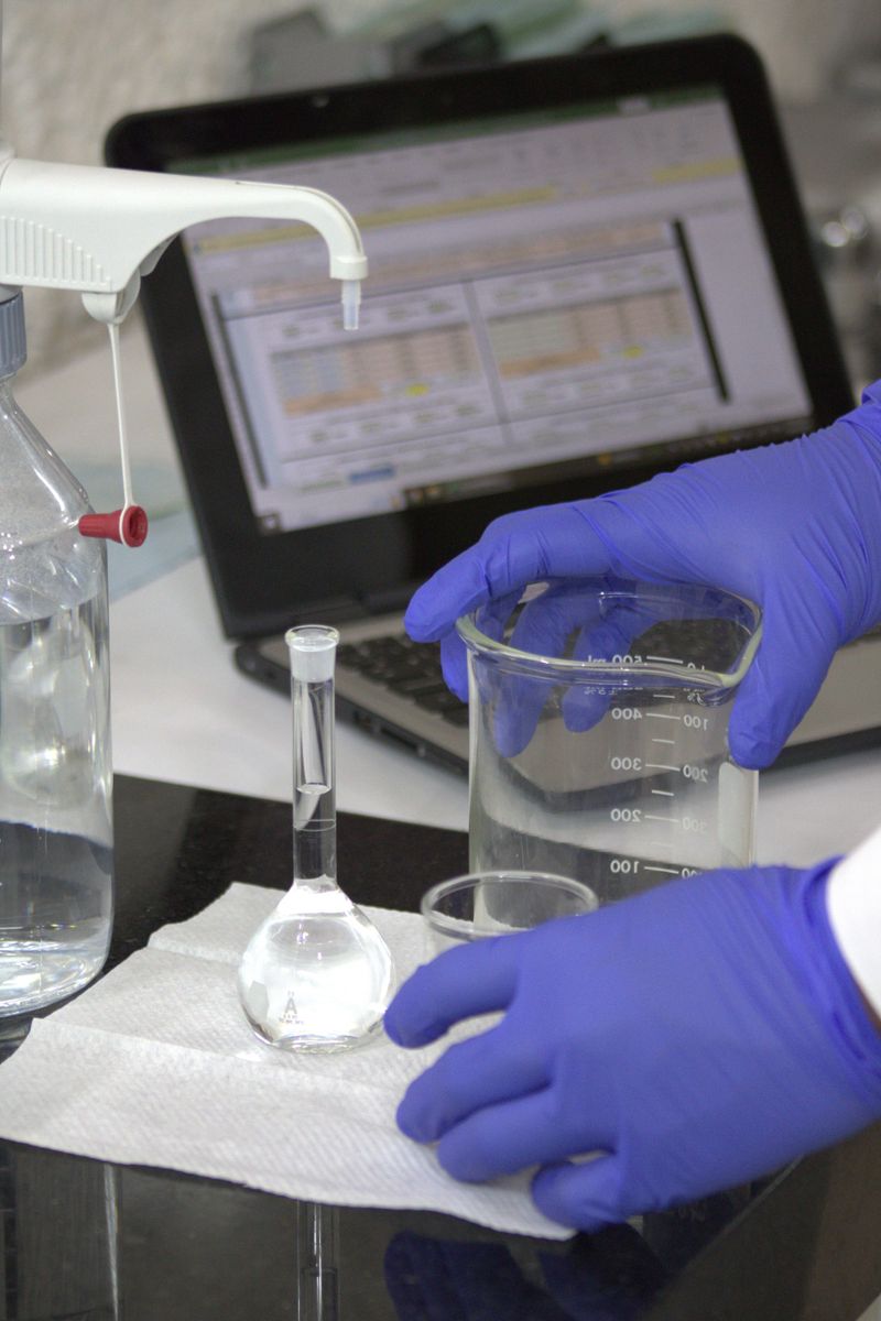 Scientist in gloves with beaker and laptop in a lab, conducting experiments.