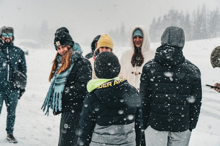 Group Of Friends With Children On A Snowy Hillside Among Falling Snow