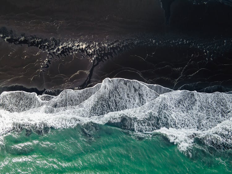 Aerial View Of Waves Crashing Onto Volcanic Sand Beach