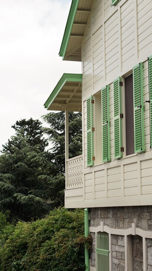 Free Side view of a wooden house with green shutters and lush greenery. Stock Photo