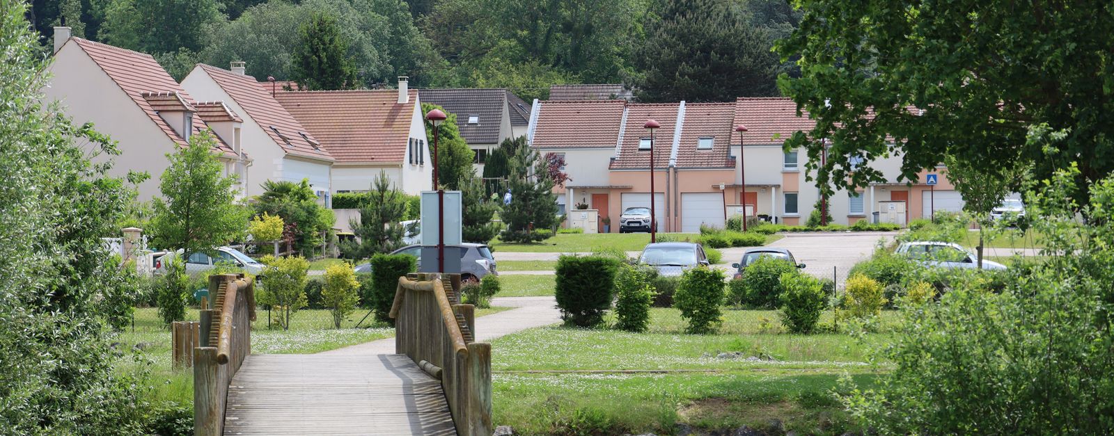 Picturesque view of a wooden footbridge leading to a peaceful village in Breuil-le-Sec, France.