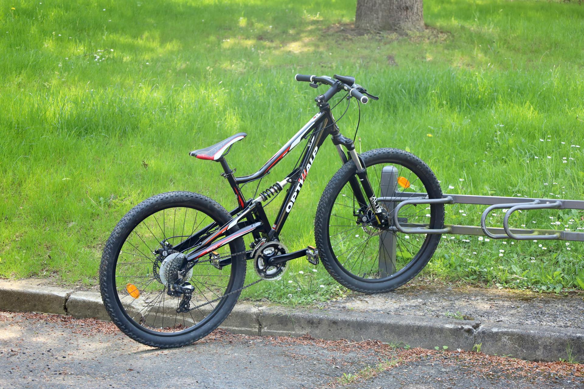 A mountain bike parked on a bike rack in a sunny urban park setting.