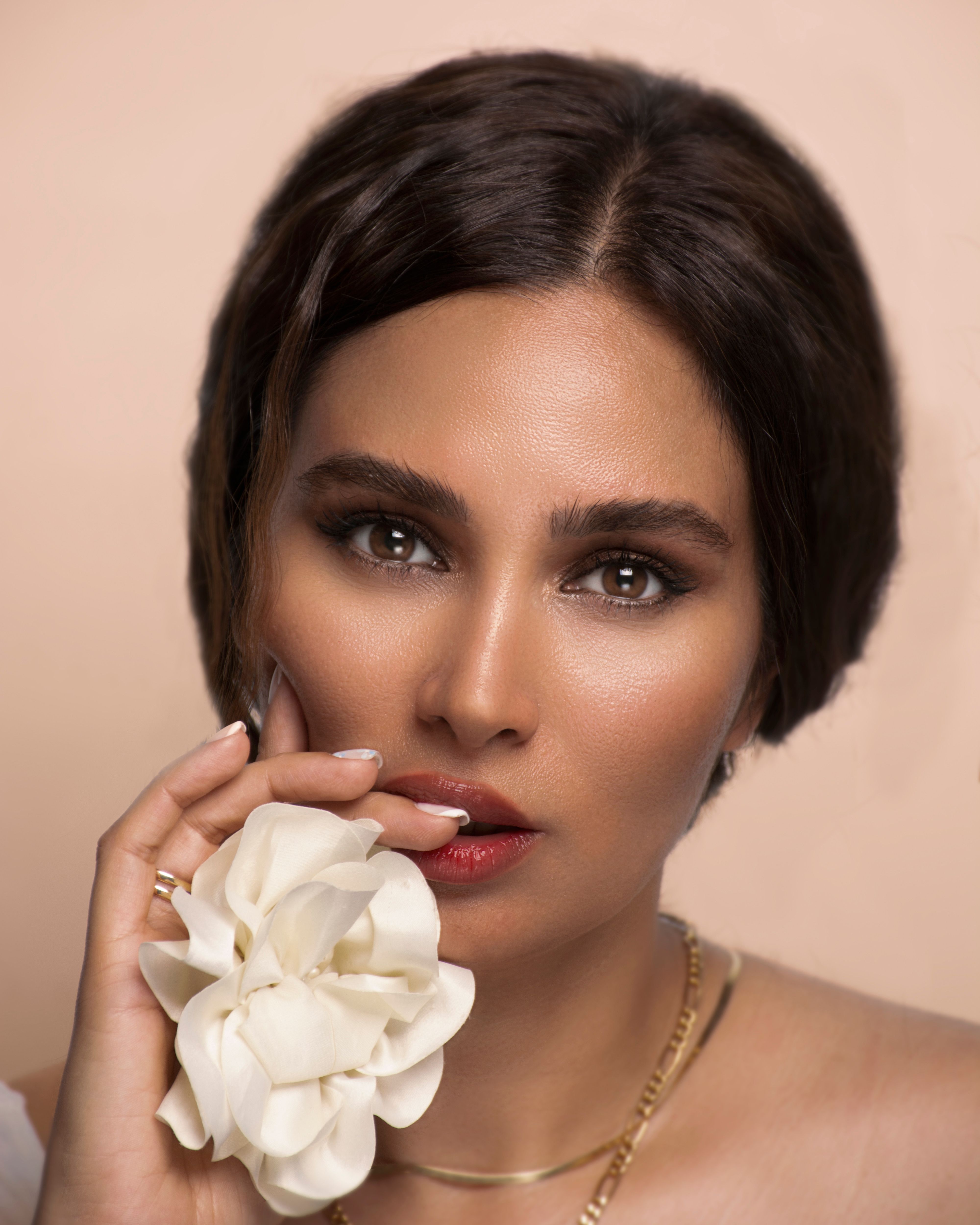 Close-up portrait of an elegant woman holding a white flower, set against a neutral background.