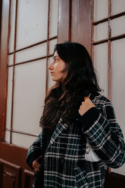 Young Brunette Wearing a Checkered Coat and Standing in front of a Building