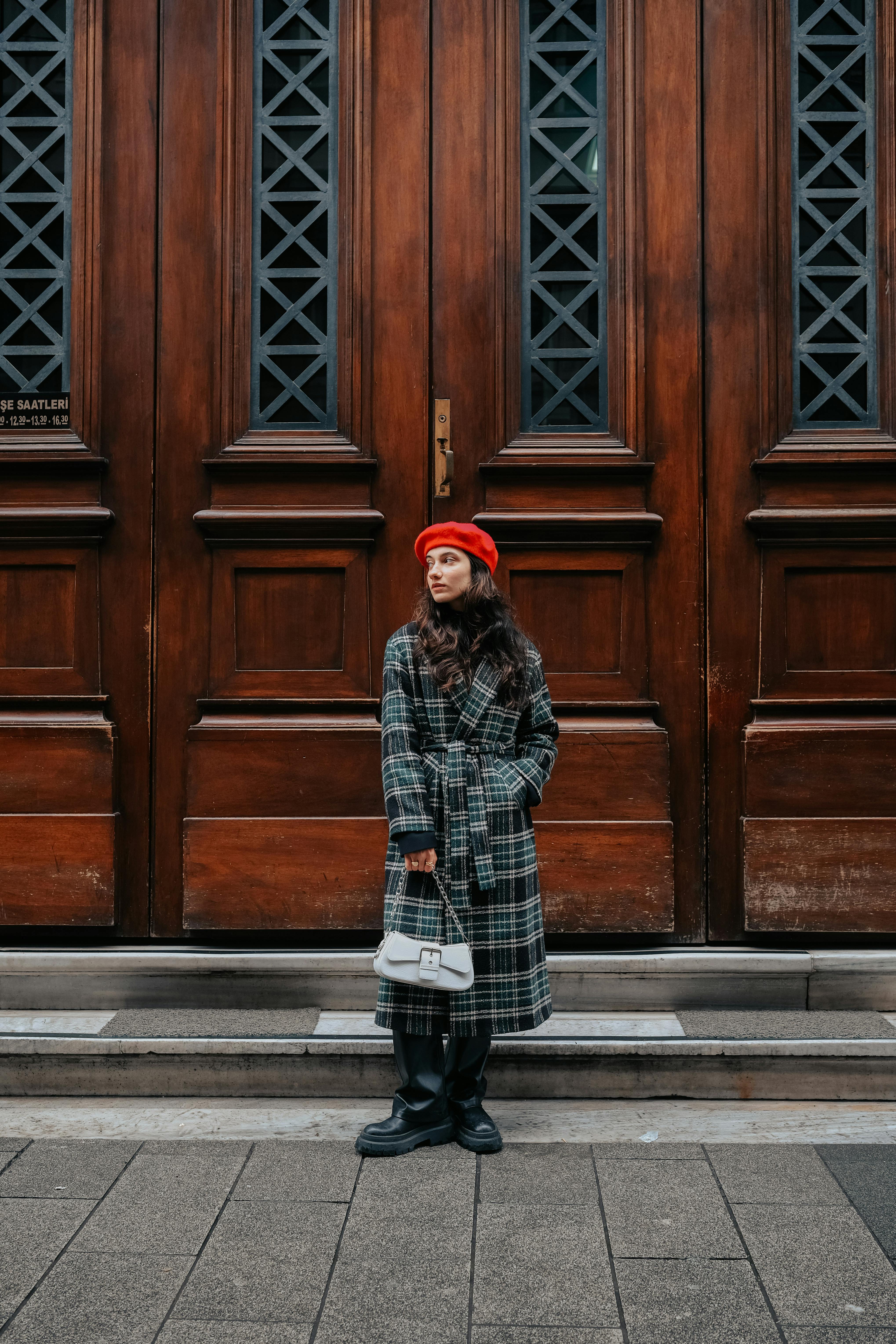 Stylish woman in a checkered coat and red beret standing by ornate wooden doors.