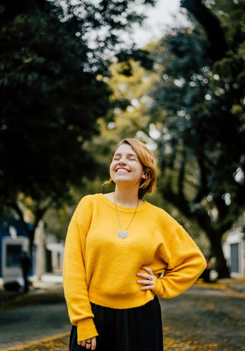 Smiling Young Woman in Yellow Sweater Standing on the Sidewalk