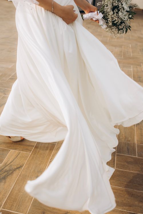 Free Graceful bride holds bouquet, walking in a flowing wedding dress outdoors. Stock Photo