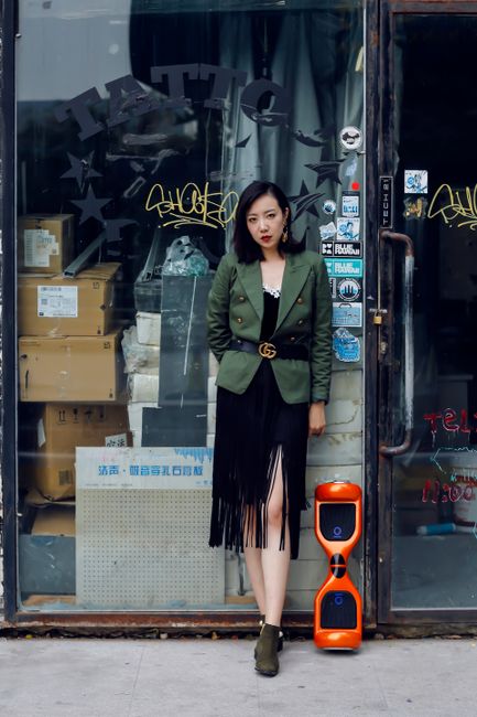Stylish woman in urban street scene wearing a green jacket and black skirt.