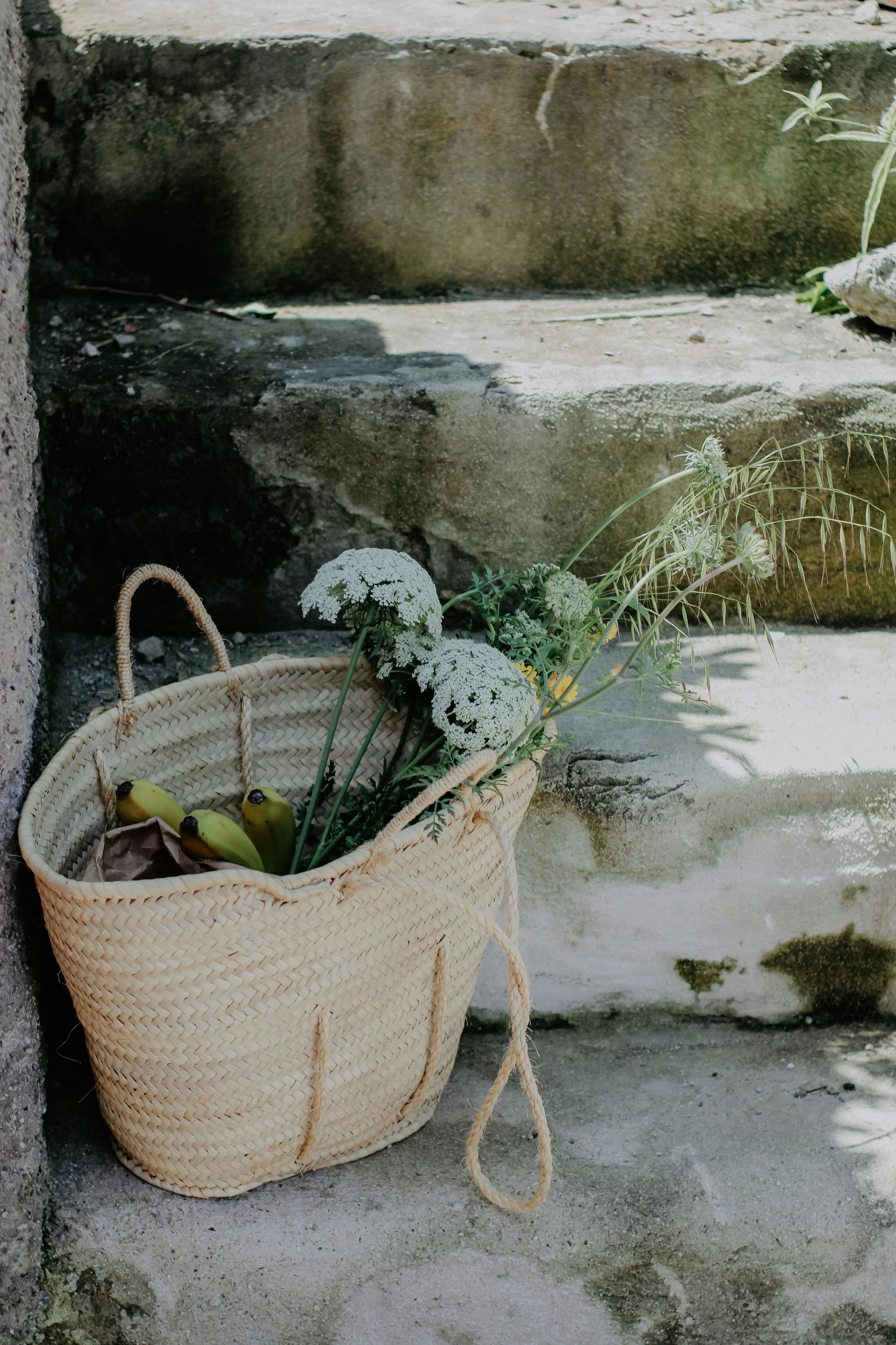 Woven basket with bananas and wildflowers placed on stone steps, capturing rustic elegance.