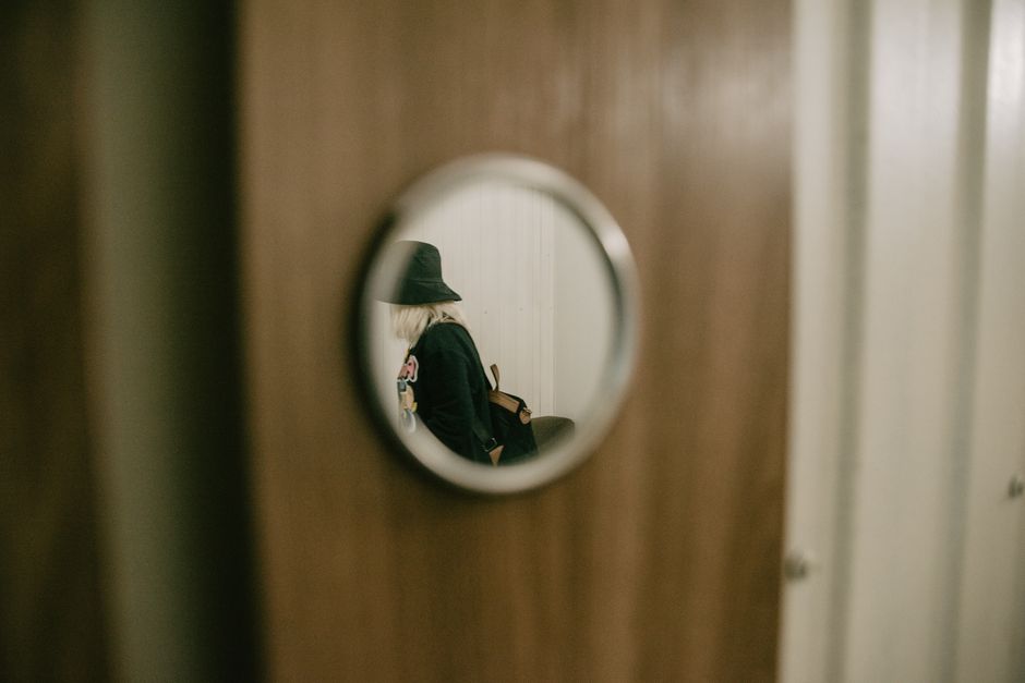 A stylish woman reflected in a circular mirror on a wooden door, indoors.