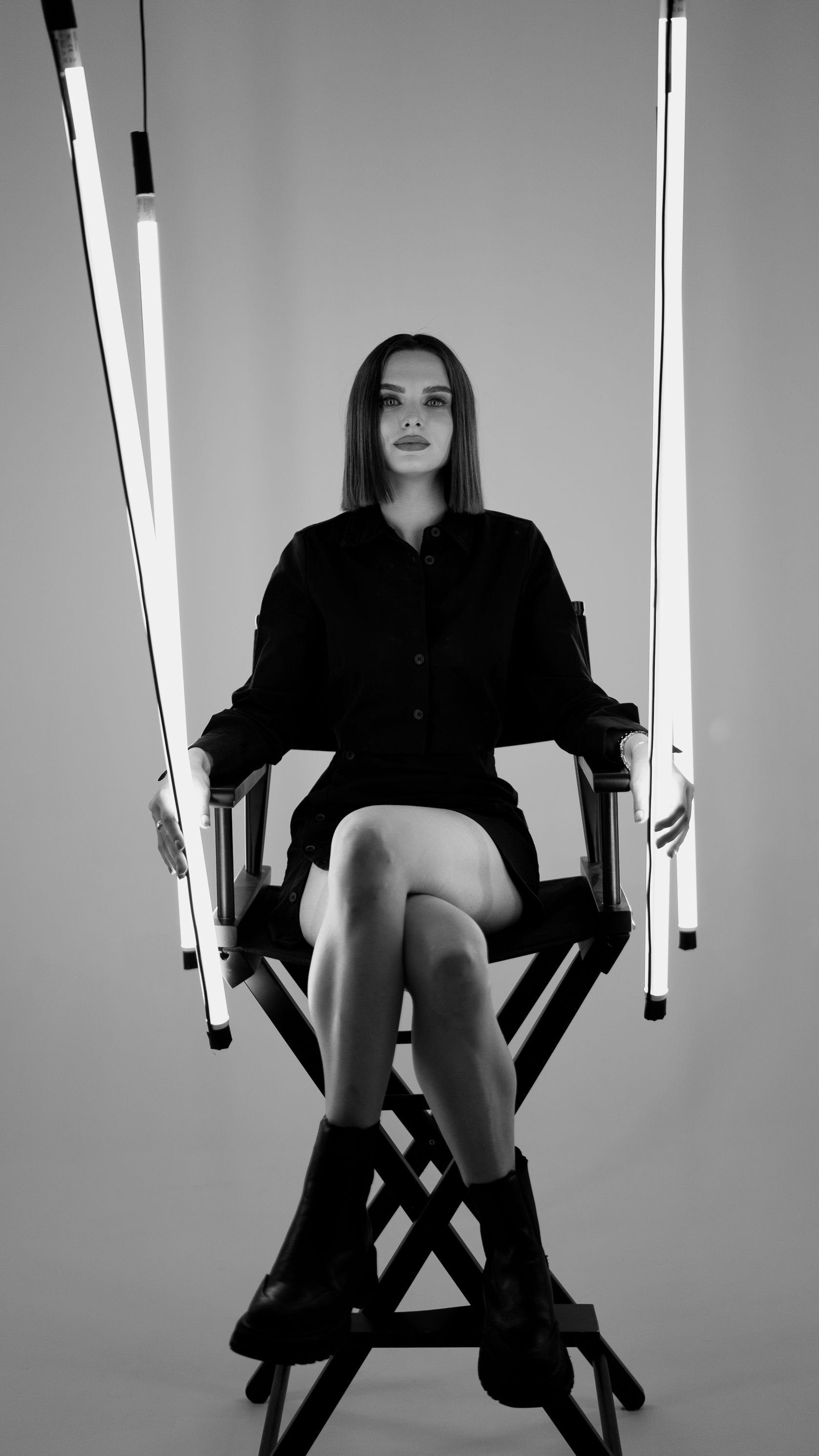 Bold black and white fashion portrait featuring a woman in black attire, seated with dramatic lights.