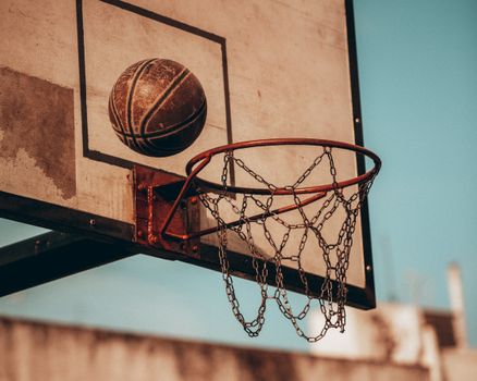 Close-up of an aged basketball hoop and ball in motion, set against a vivid sky in Buenos Aires.