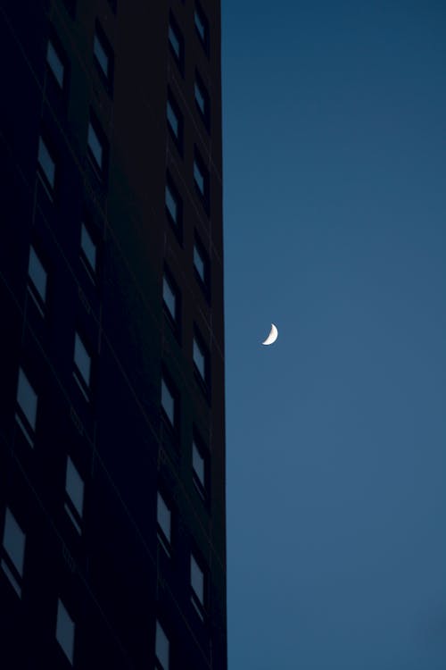 View of an Apartment Block and Crescent Moon at Dusk 
