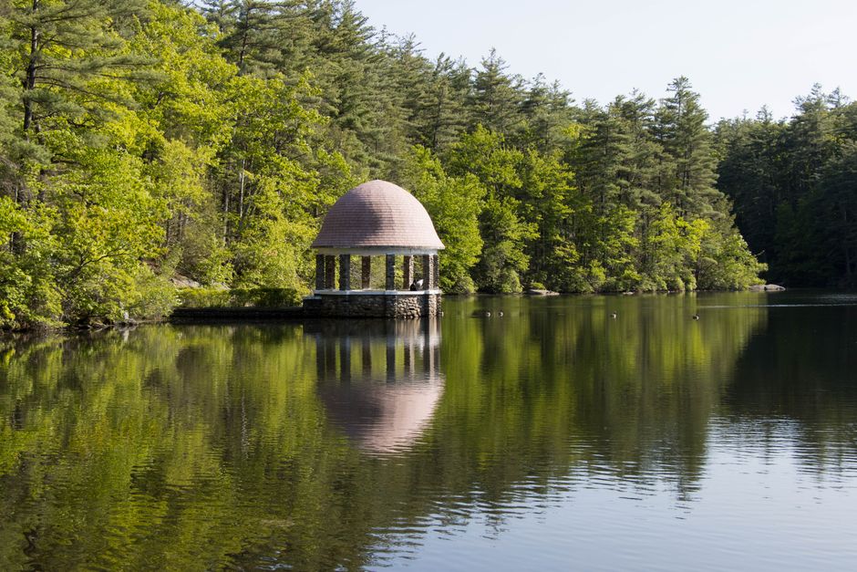 Tranquil scene of a gazebo reflecting in a pond surrounded by lush trees in Fitchburg, MA.