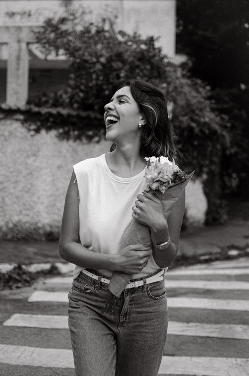 Free Young woman joyfully carrying flowers on a city crosswalk, captured in black and white. Stock Photo