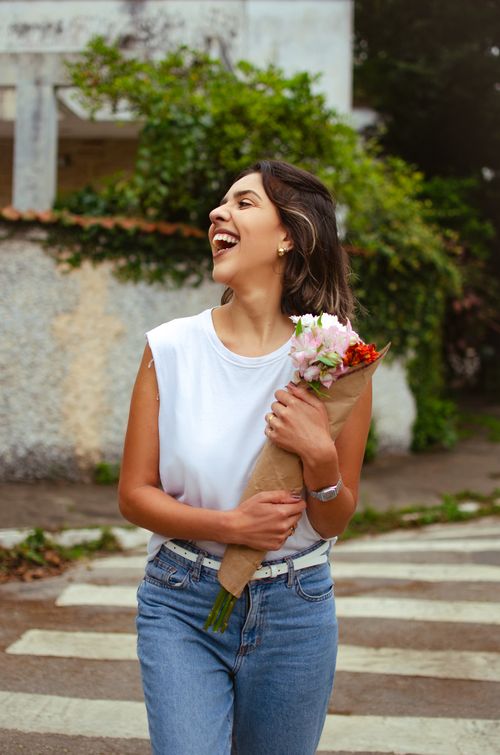 Free Happy woman in casual outfit walking outdoors with a bouquet of flowers, embodying a joyful summer vibe. Stock Photo