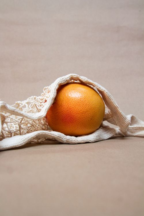 Free A fresh grapefruit nestled in a textured cotton bag against a neutral beige backdrop. Stock Photo