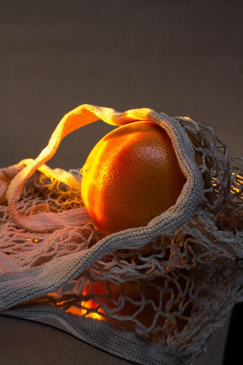 Free A ripe grapefruit illuminated with warm light in a reusable net bag, symbolizing eco-friendly living. Stock Photo