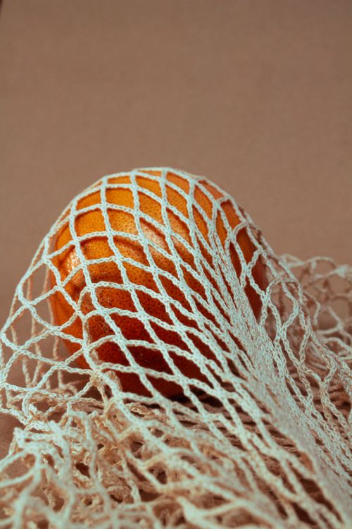 Free A detailed view of a fresh orange partially wrapped in netted fabric, showcasing texture and color. Stock Photo