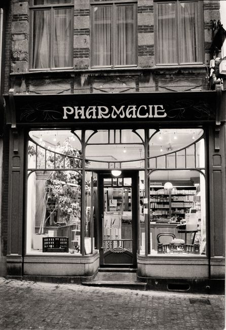 Black and white image of a vintage pharmacy storefront with charming facade and display.