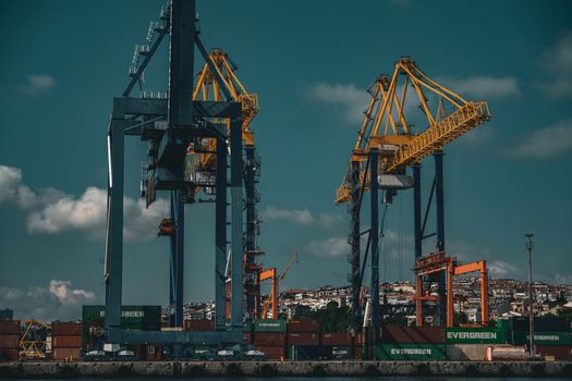 Industrial cranes at the bustling İstanbul port with shipping containers under a clear blue sky.