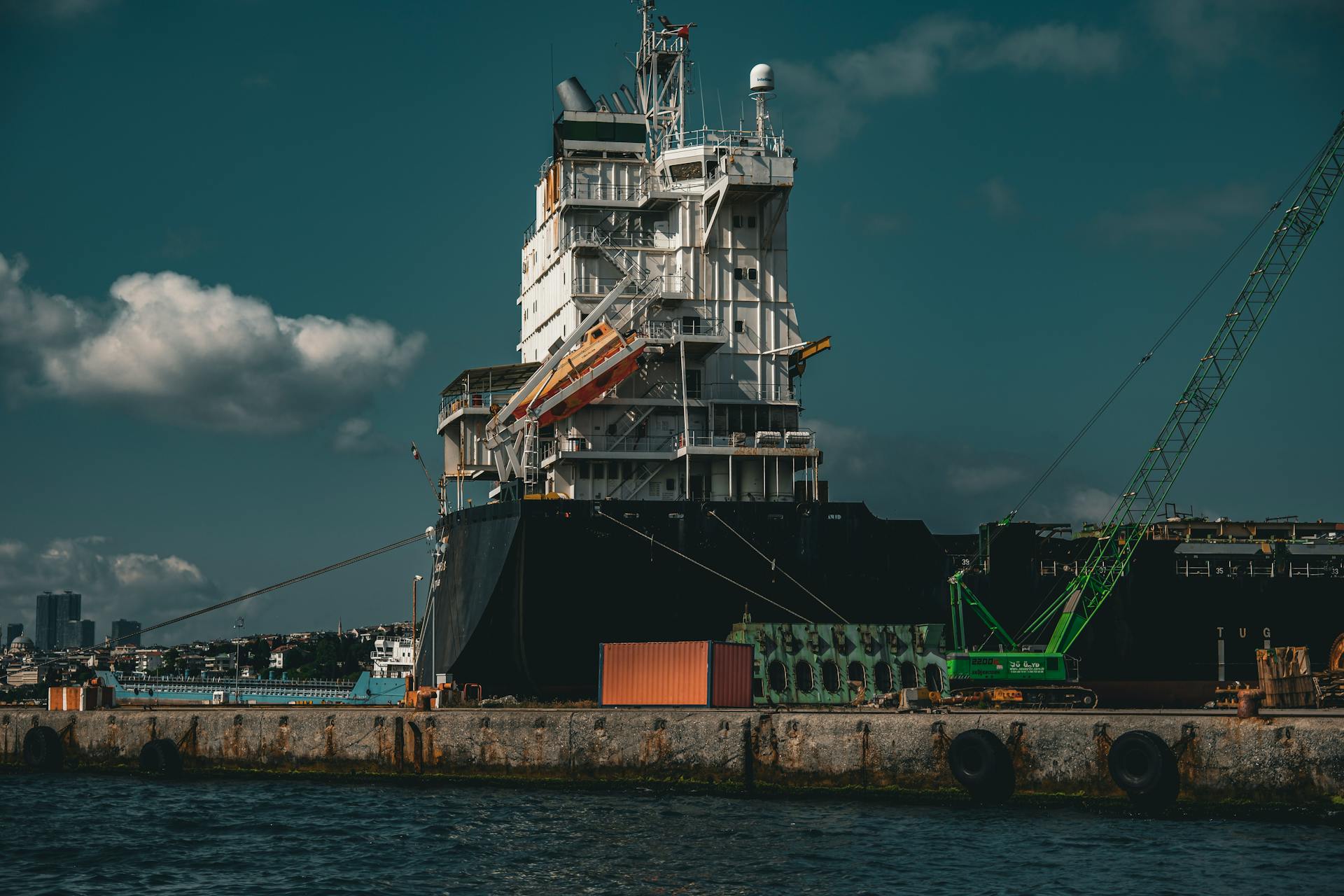 Large cargo ship with cranes docked at İstanbul harbor under a dramatic sky.