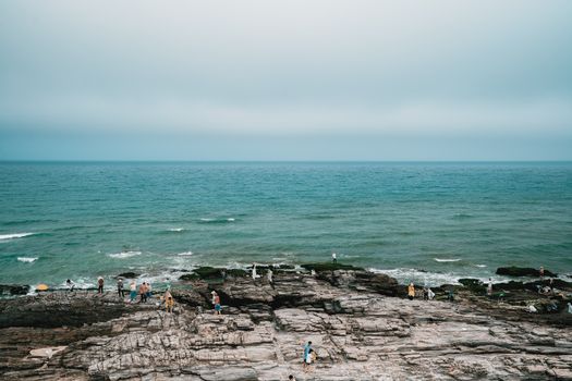 Visitors explore a rocky coastline under a serene sky and calm sea waves.