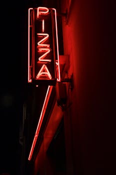 A vivid neon pizza sign glowing in the night on a Paris street.