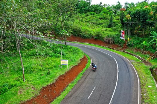 Motorcyclist navigating a lush green curve on Cikidang road, West Java, Indonesia.