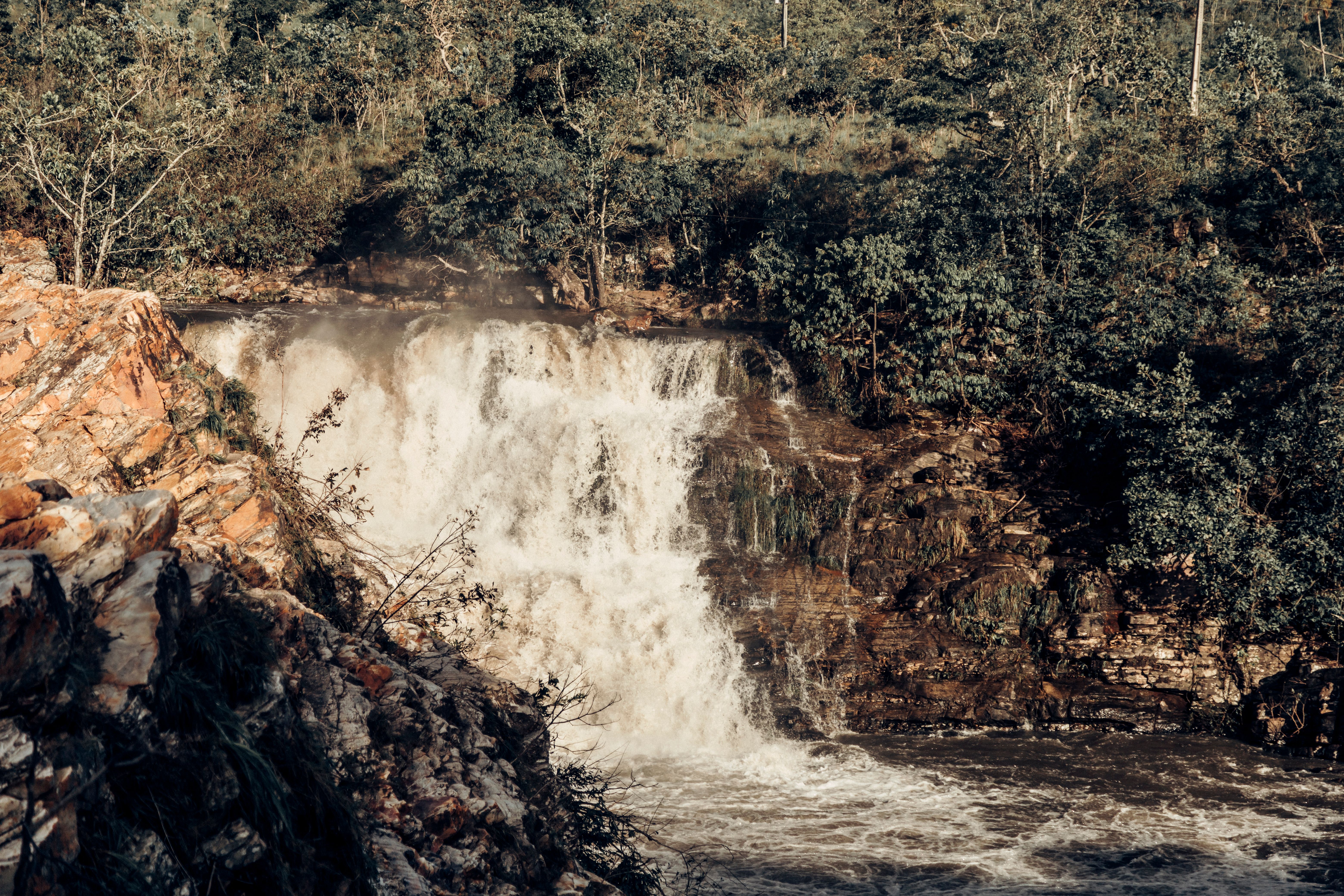 A picturesque waterfall flowing through a forested area with rocky cliffs and abundant greenery.