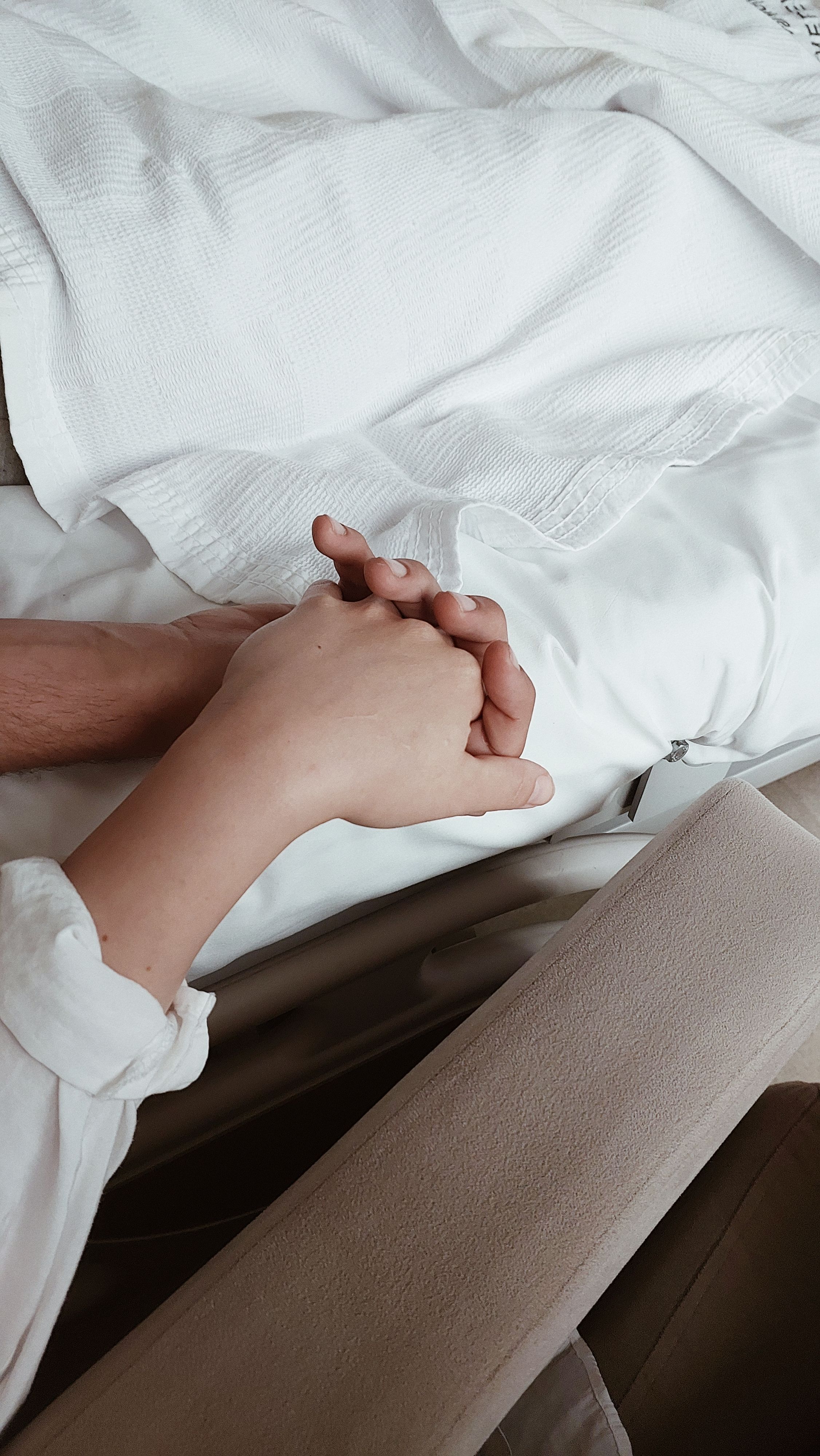 Close-up of two hands holding on a bed, symbolizing intimacy and support.